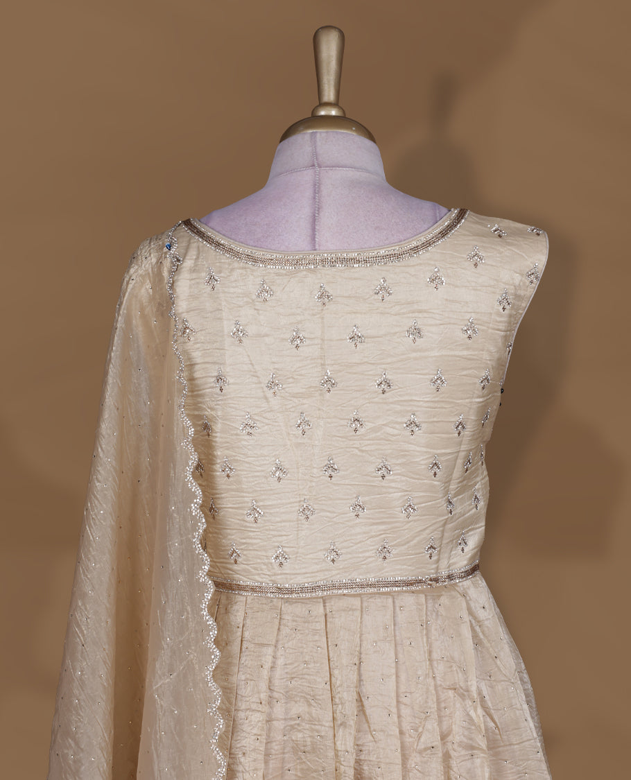 Champagne beige colour stitched gown set with sleeveless embroidered yoke, flared ankle‑length silhouette, and attached dupatta featuring delicate butti work and scalloped beaded edging.