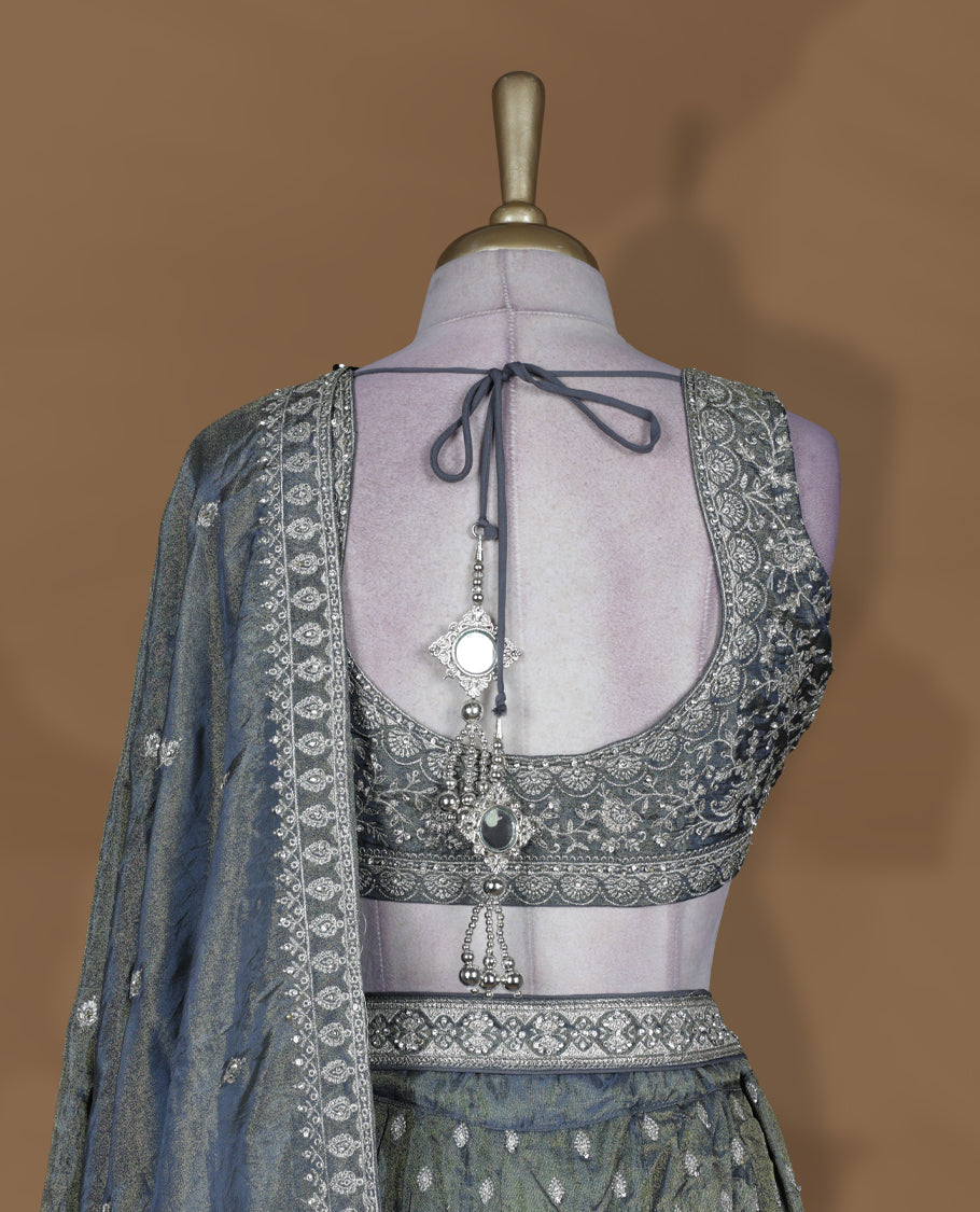 Steel grey and olive ombre effect lehenga set with stitched sleeveless V‑neck embroidered blouse, matching stitched flared lehenga featuring heavy zari and sequin work, and coordinated dupatta with embellished border.
