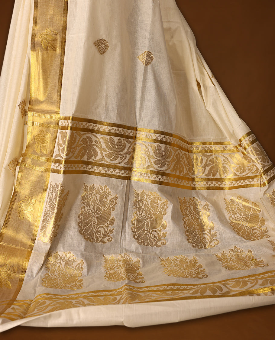Elegant off white colour cotton Kerala saree embellished with golden buttas across the body and an ornate golden zari border and pallu featuring intricate motifs & A perfect traditional pick, paired with a matching blouse piece.