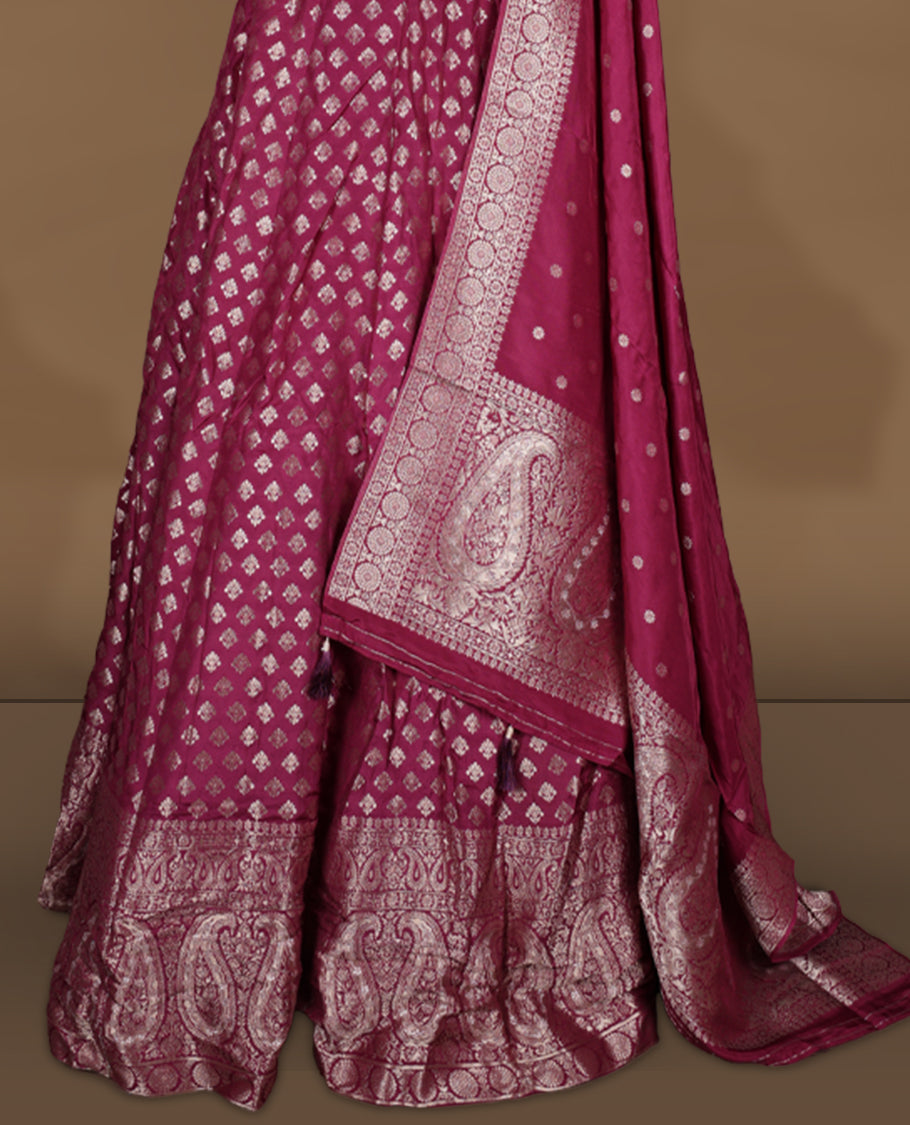 Wine colour Banarasi lehenga set with a stitched flared lehenga featuring all‑over zari butti motifs and rich woven border, paired with an unstitched floral zari blouse piece and matching dupatta with zari border and tasselled edges.