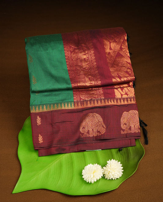 Green colour kalyani cotton saree featuring gold zari motifs on body, complemented by contrast maroon color with copper zari elephant pattern border , paired with matching blouse piece.