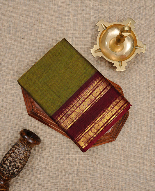 Dark olive colour Chettinad cotton saree featuring Elegant plain body, complemented by contrast Maroon colour with gold zari border, paired with matching blouse piece.