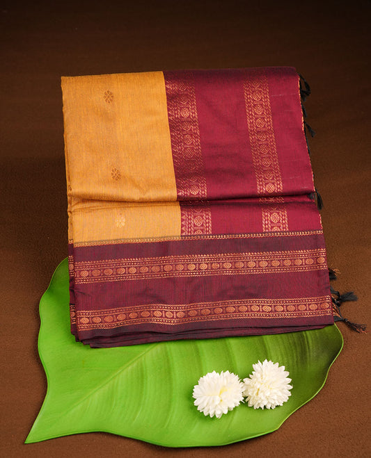 Mustard colour kalyani cotton saree featuring gold zari motifs on body, complemented by contrast maroon color with copper zari pattern border , paired with mtaching blouse piece.