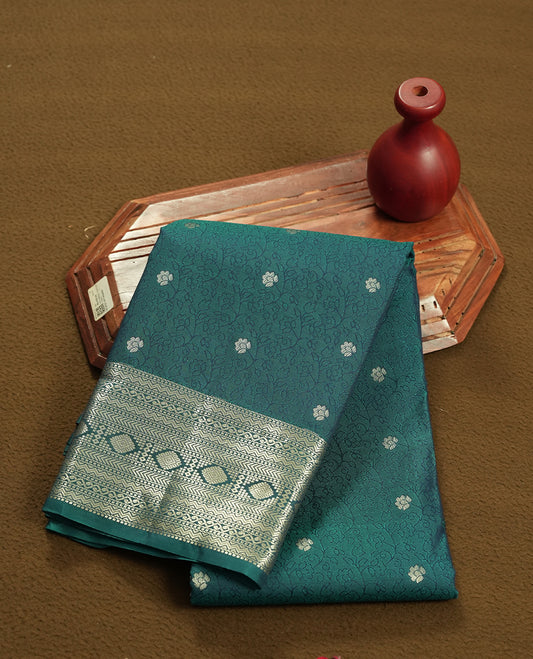 Teal Green colour semi soft silk saree featuring a self coloured textured with golden patterned body, complemented by self coloured golden zari motifes on pallu & border and a matching blouse piece.