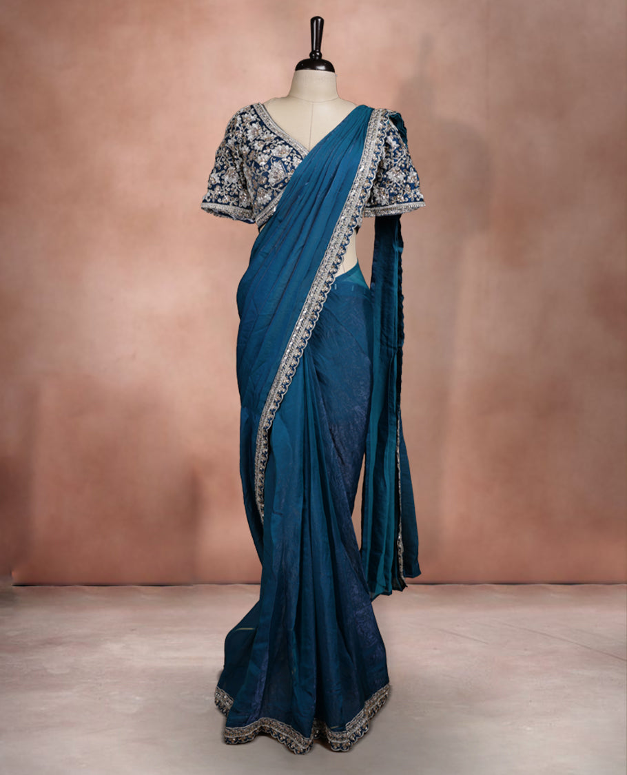 Elegant Teal Blue Colour ready to wear saree adorned with rich silver zari and bead embroidery along the border and pallu, paired with a heavily embellished matching blouse for a grand festive look.