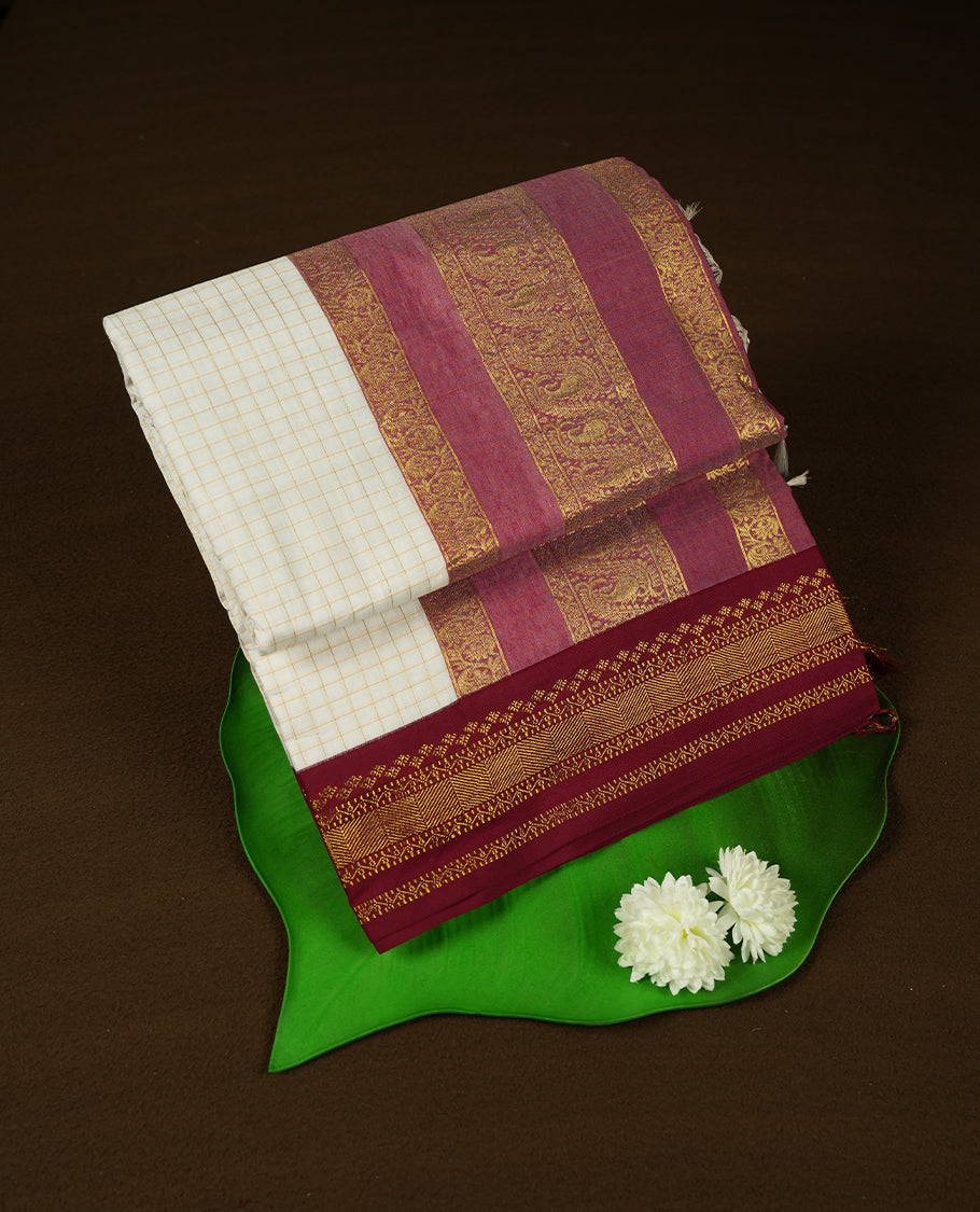 Off white coloured mixed Kalyani cotton saree featuring copper zari checks on the body, complemented by a maroon red coloured border and pallu adorned with golden zari patterns, Paired with a matching blouse.