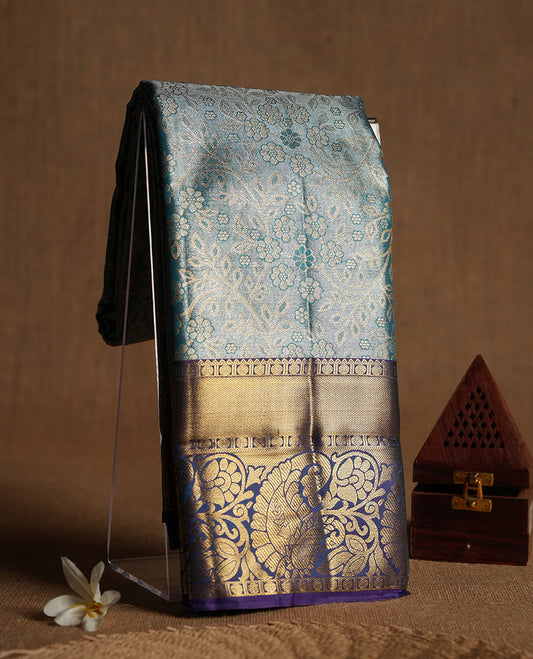 Blue colour tissue brocade saree with delicate floral and leaf motifs in antique gold zari work throughout body. Ornate gold border and pallu with traditional floral scrolls, navy blue accents. Includes coordinating blouse.