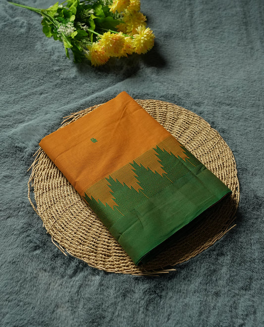 Burnt Mustard Colour silk cotton saree with tiny emerald thread buttas, temple green serrated borders, a pallu lined with green stripes, paired with a plain burnt mustard blouse featuring the same temple green border
