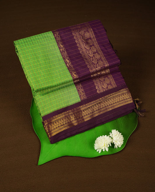 Bright Green coloured mixed Kalyani cotton saree featuring golden zari checks on the body, complemented by a rich grape coloured border and pallu adorned with golden zari patterns, Paired with a matching blouse.