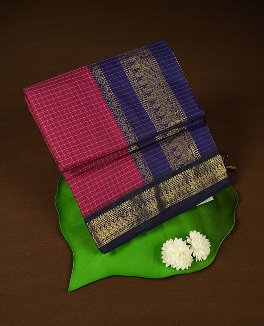 Burnt maroon coloured mixed Kalyani cotton saree featuring golden zari checks on the body, complemented by a dark royal blue coloured border and pallu adorned with golden zari patterns, Paired with a matching blouse.