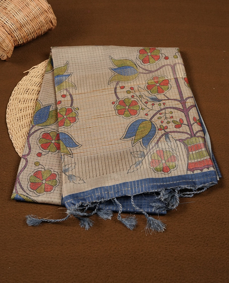 Wheat colour semi tussar silk saree featuring floral print and check pattern across body, contrast blue colour border and pallu, paired with matching blouse piece.