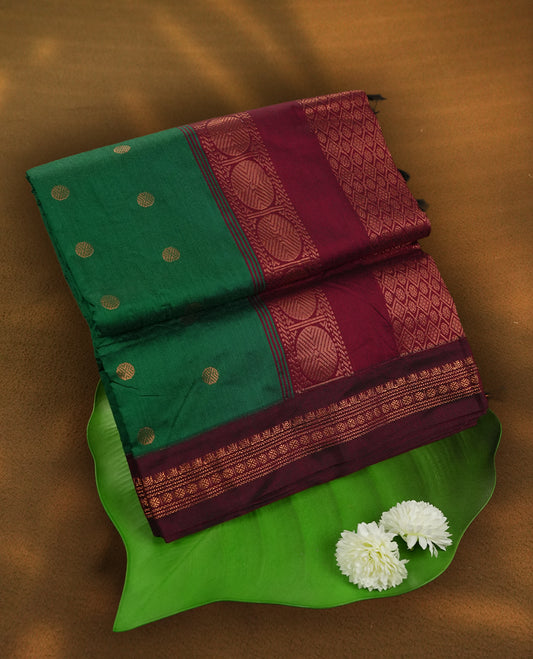 Green colour Kalyani Cotton saree with golden motifs, paired with a contrasting maroon border featuring intricate zari work & Comes with a matching blouse piece.