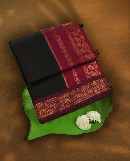 Black colour Kalyani Cotton saree in deep maroon with golden motifs, paired with a contrasting maroon border featuring intricate zari work & Comes with a matching blouse piece,