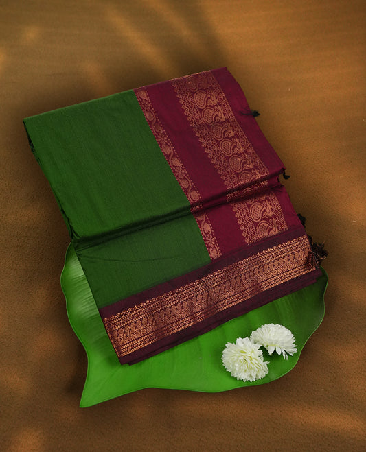 Deep forest green colour Kalyani Cotton saree with rich maroon border and pallu, featuring copper zari peacock motifs and intricate weaving & Includes a matching blouse piece.