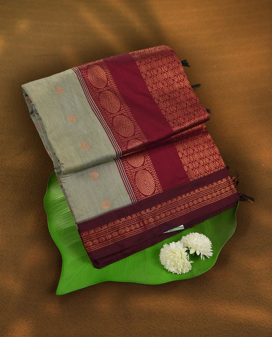 Grey colour Kalyani Cotton saree in deep maroon with golden motifs, paired with a contrasting maroon border featuring intricate zari work & Comes with a matching blouse piece.