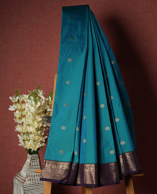 Teal Blue Colour Semi Silk Saree with Golden Peacock Butta Motifs, Contrasting Purple Golden Zari Pallu & Border, Traditional Leaf Designs, and Matching Blouse Piece