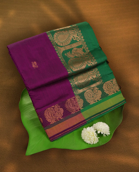 Purple colour Kalyani Cotton saree in deep green with golden peacock motifs, paired with a contrasting green border featuring intricate zari work & Comes with a matching blouse piece.