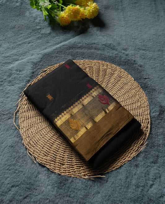 Black Colour silk cotton saree with scattered pink and orange buttas, gold and bronze temple border with pink floral band, gold zari pallu with leaf patterns, black blouse with bronze border.