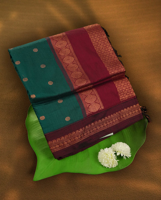 Teal green Kalyani cotton saree with contrast maroon border highlighted by rich golden zari weaving and elegant buttas on the body & Comes with blouse.