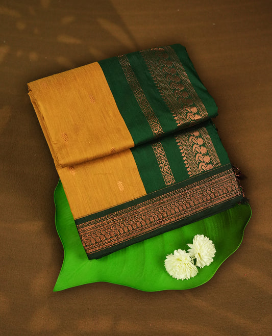 Mustard yellow colour Kalyani Cotton saree with woven zari motifs all over, paired with a contrasting green border and pallu intricately woven with copper zari & Comes with a matching blouse piece.