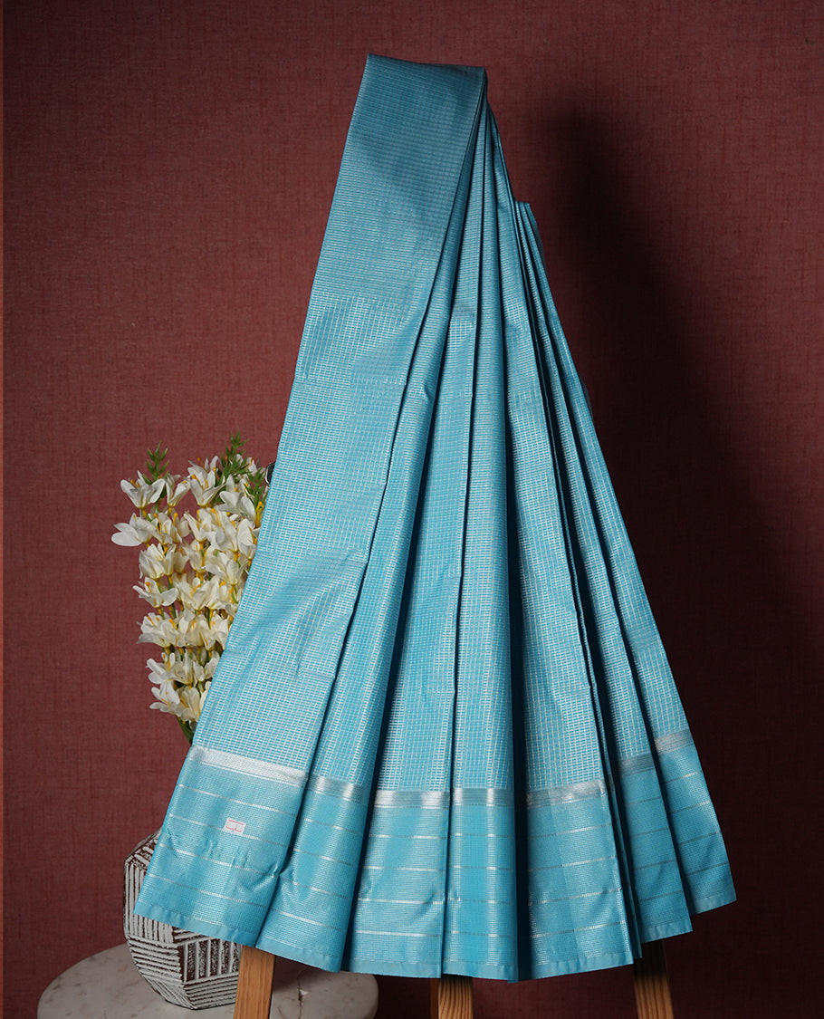 Bright light blue colour Semi Silk Saree with silver zari checks on the body, complemented by a self coloured pallu and border woven in silver zari, paired with a matching blouse piece.
