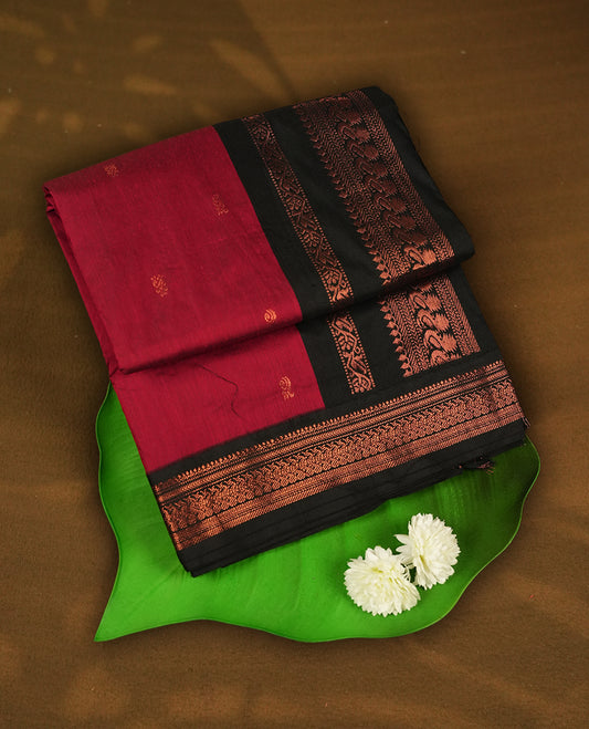 Deep maroon colour Kalyani cotton saree featuring delicate zari motifs work on the body, highlighted with an elegant contrast black zari woven border & Paired with a matching blouse.