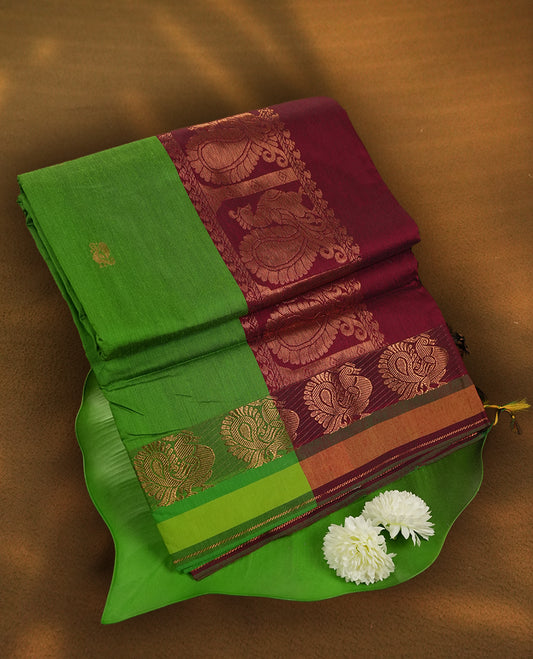 Parrot green colour Kalyani Cotton saree in deep maroon with golden peacock motifs, paired with a contrasting maroon border featuring intricate peacock zari work & Comes with a matching blouse piece.
