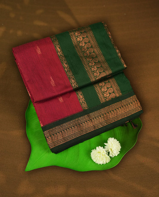 Maroon colour Kalyani cotton saree with subtle zari motifs all over, paired with a contrasting green rich copper zari woven border and pallu & comes with a matching blouse piece.