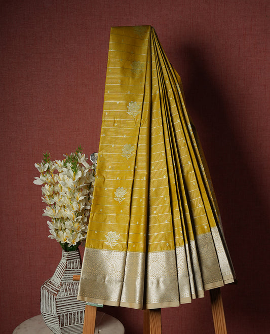 Light olive yellow colour Semi Silk Saree featuring silver zari floral motifs on the body, complemented by a muted brown traditional pallu and border, and paired with a matching blouse piece.