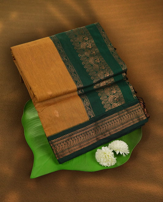 Mustard yellow colour Kalyani Cotton saree with golden motifs, paired with a contrasting green border featuring intricate peacock zari work & Comes with a matching blouse piece.
