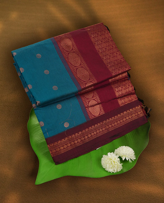 Blue colour Kalyani Cotton saree in deep maroon with golden motifs, paired with a contrasting maroon border featuring intricate zari work & Comes with a matching blouse piece,