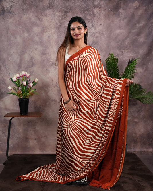 Rust Orange Colour satin model saree featuring Zibra print on body. Ajrak & zibra print on pallu with jhumka tassels, comes with contrast plain blouse piece.