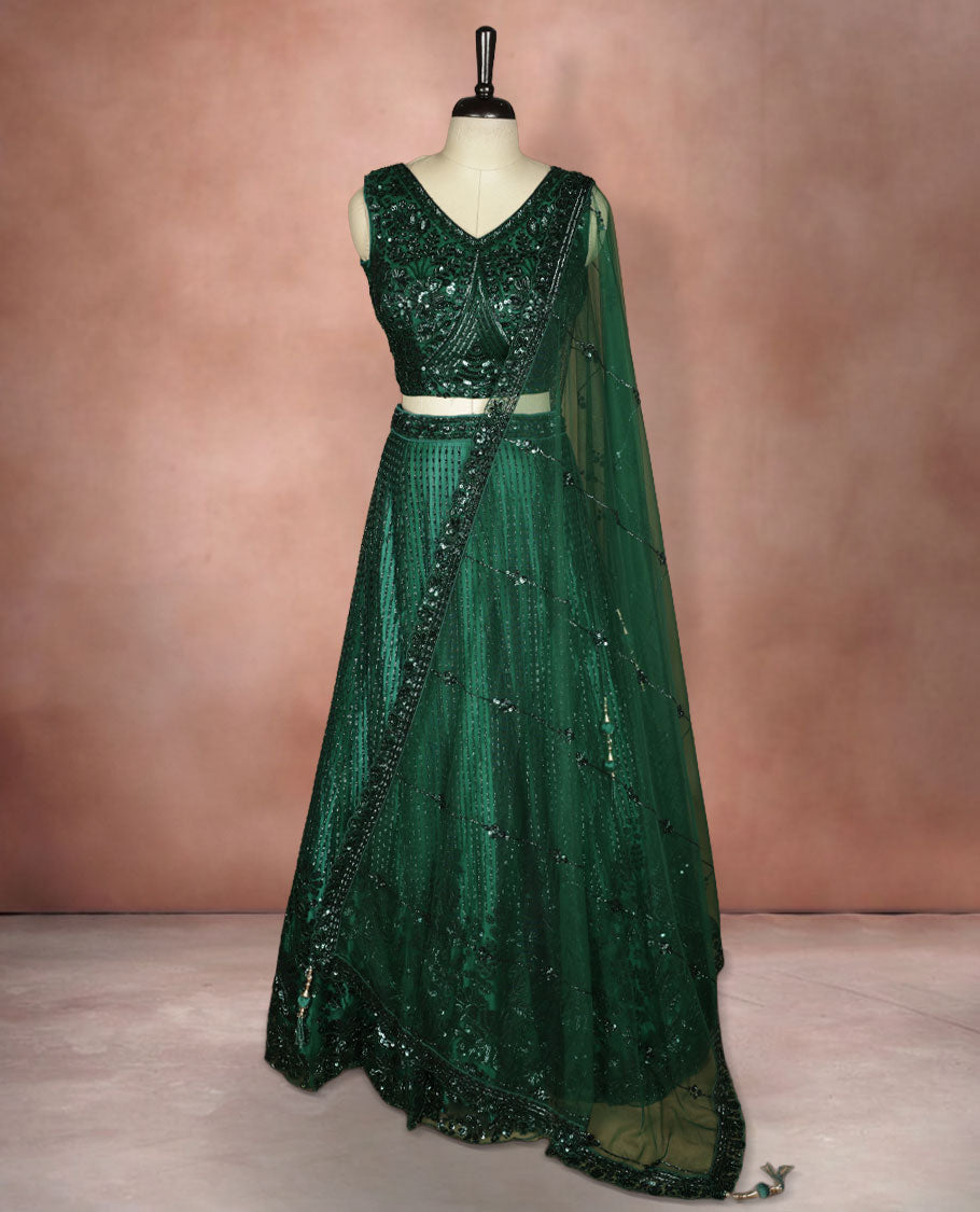 Emerald green colour lehenga set with stitched sleeveless V‑neck heavily sequinned blouse featuring cut‑out tie‑up back, matching stitched flared lehenga, and net dupatta with sequin border and scattered floral motifs.