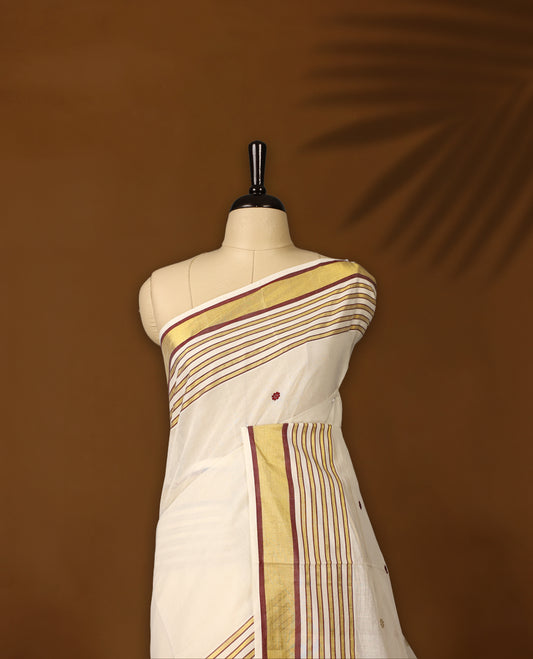 Off white colour pure handloom soft cotton kerala saree with maroon and mustard polka motifs, highlighted by a golden zari border and striped pallu in gold, maroon, and green, and paired with a matching blouse, perfect for festivities.