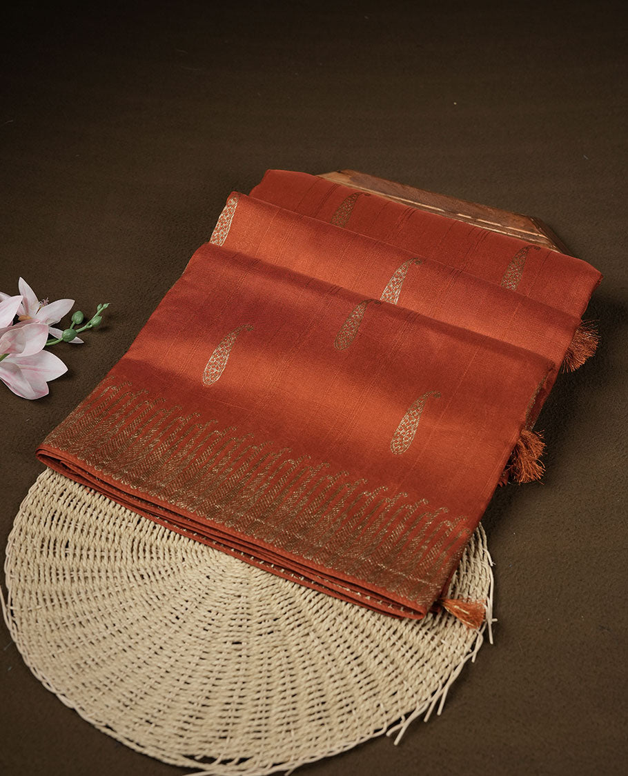 Burnt orange colour semi banaras tussar georgette featuring gold zari leaf pattern across body, finished with gold zari border and paired with matching blouse.