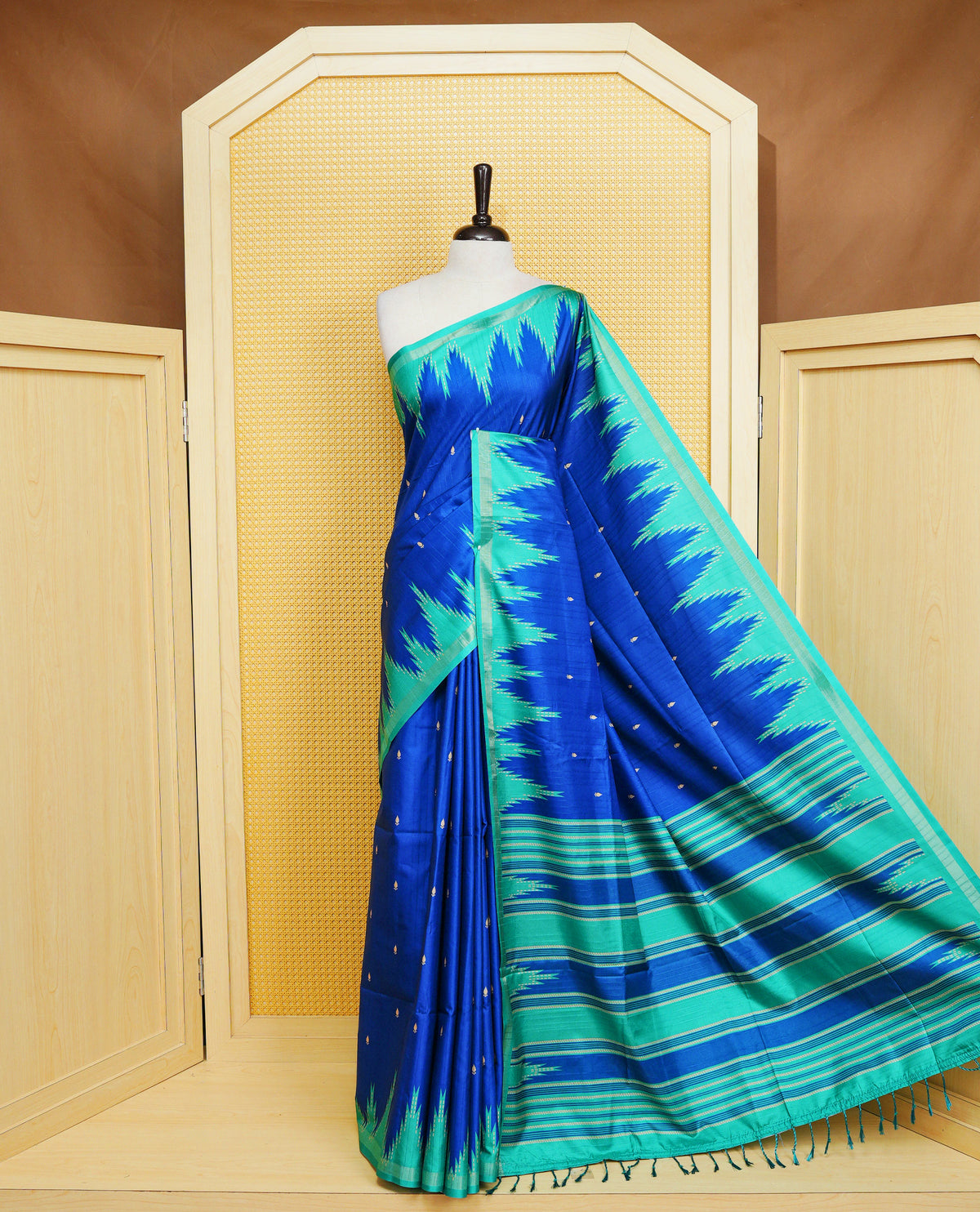 Royal Blue and Teal Green Colour Kattan silk saree featuring buttas all over the body, a temple-designed border &  a contrasting striped pallu with tassels. Paired with a matching contrast-striped blouse piece.
