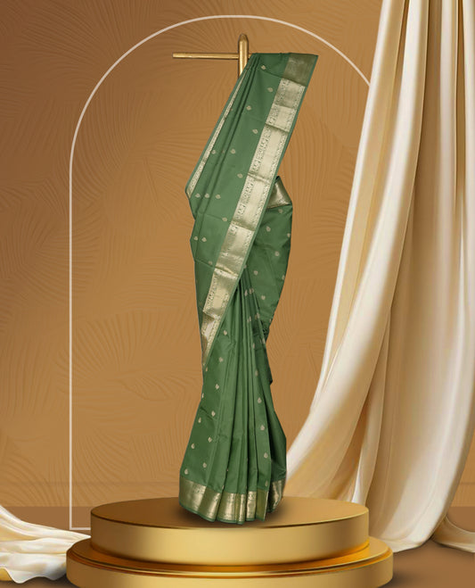 Dark pista green colour soft silk saree adorned with small golden buttas, enhanced by a shimmering gold zari border and pallu with delicate motifs & Paired with a matching blouse.