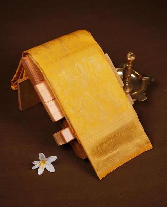 Mustard yellow colour semi soft silk brocade saree featuring subtle self-woven paisley motifs on the body, finished with an intricately woven matching border and pallu, paired with a coordinating blouse piece.