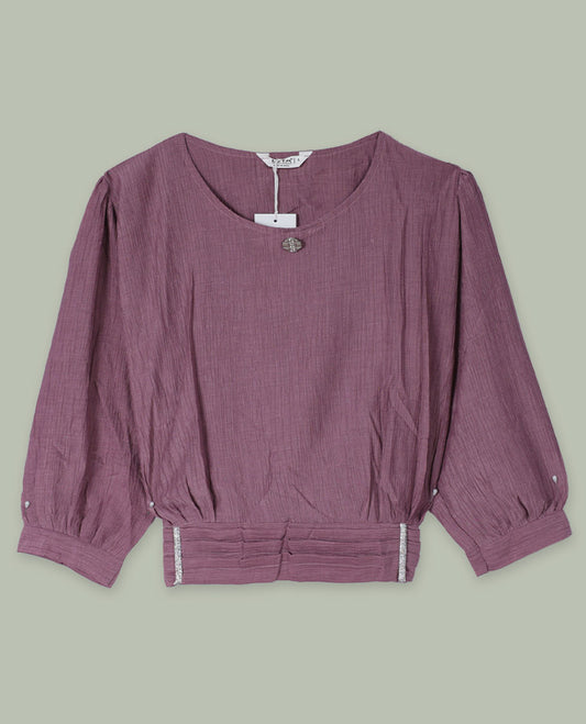 Dusty mauve three-quarter sleeve top with round neckline, metal button detail at the neck, and a pleated waistband accented with slim metallic trims.