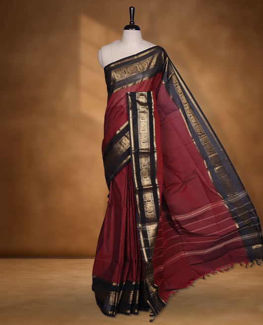 Maroon colour chettinad cotton saree featuring plain body, contrast black colour with traditional gold zari border paired with matching blouse.
