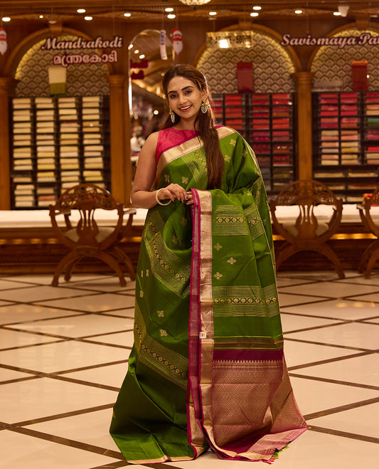 Vibrant parrot green colour Kancheepuram silk saree adorned with delicate gold zari motifs across the body, beautifully complemented by a classic zari border with hints of contrast, styled with a blouse