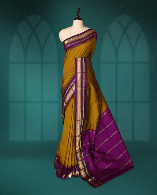 Mustard yellow semi silk saree with plain body, royal ourole pallu and matching purple border adorned with golden zari, accented with temple motifs along the edges, Paired with a matching blouse, perfect for festive occasions.