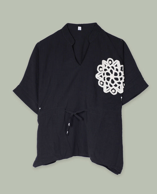 Black short-sleeve top with V-slit band neckline, contrast ivory crochet motif on one side, and adjustable drawstring detail at the waist.