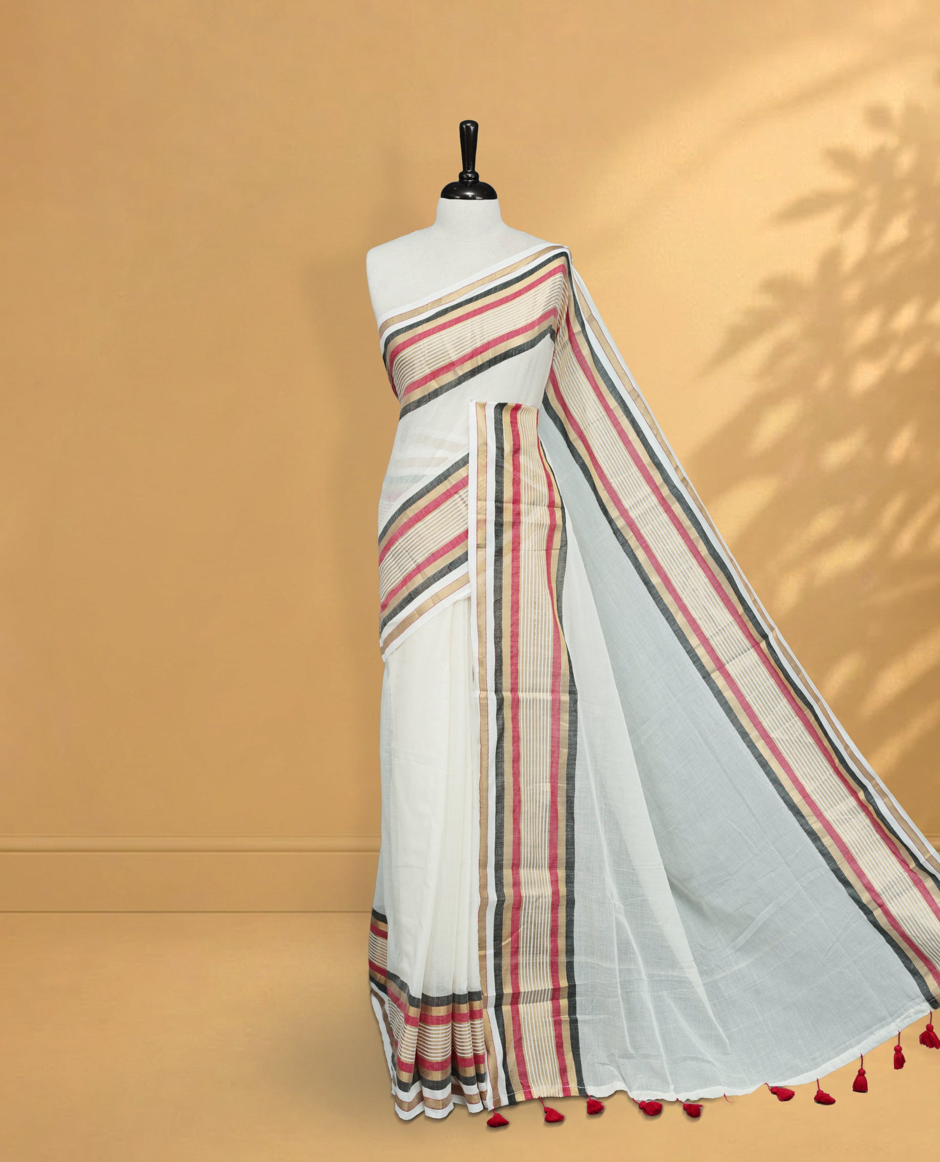 Off White Colour Mul Cotton Saree featuring Elegant Plain Body, Contrast Gold, Red & black Border and Tassels Onam inspired charm.