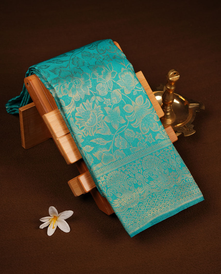 Teal green colour semi soft silk brocade saree featuring elegant self-woven floral motifs on the body, finished with an intricately detailed matching border and pallu, paired with a coordinated blouse piece.