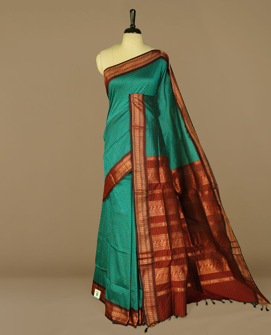 Teal green colour kalyani cotton saree featuring gold zari check pattern on body, complemented by Maroon colour with Antique zari border, paired with matching blouse piece.