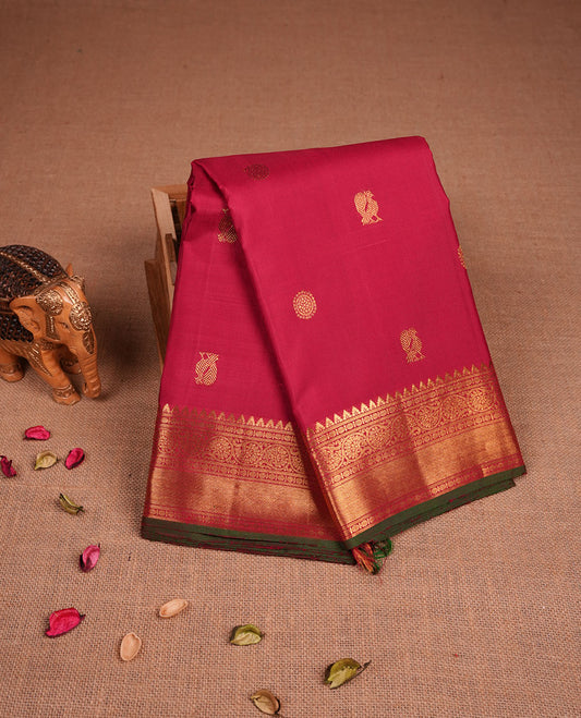 Dark red colour pure traditional Kancheepuram silk saree adorned with elegant zari peacock and chakra motifs on the body, complemented by a simple Gold Zari zari woven border, paired with a matching blouse piece.