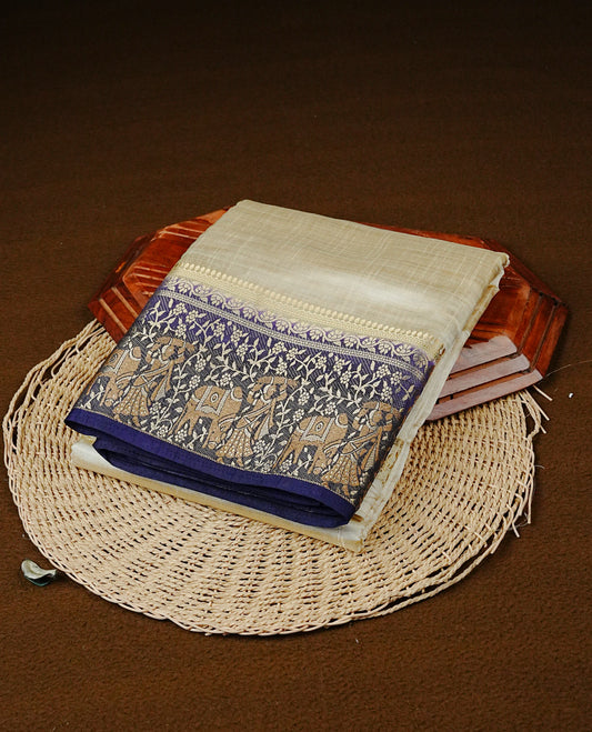 Light gold tussar saree featuring Elegant plain body, complemented by contrast Navy Blue colour with Gold zari Floral kodi with Women & Cow Pattern border, comes with matching blouse piece.