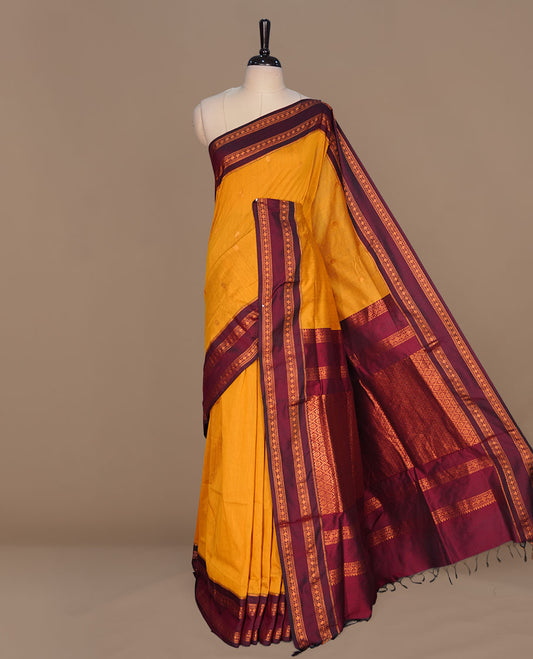 Mustard colour kalyani cotton saree featuring gold zari motifs on body, complemented by contrast maroon color with copper zari pattern border , paired with mtaching blouse piece.