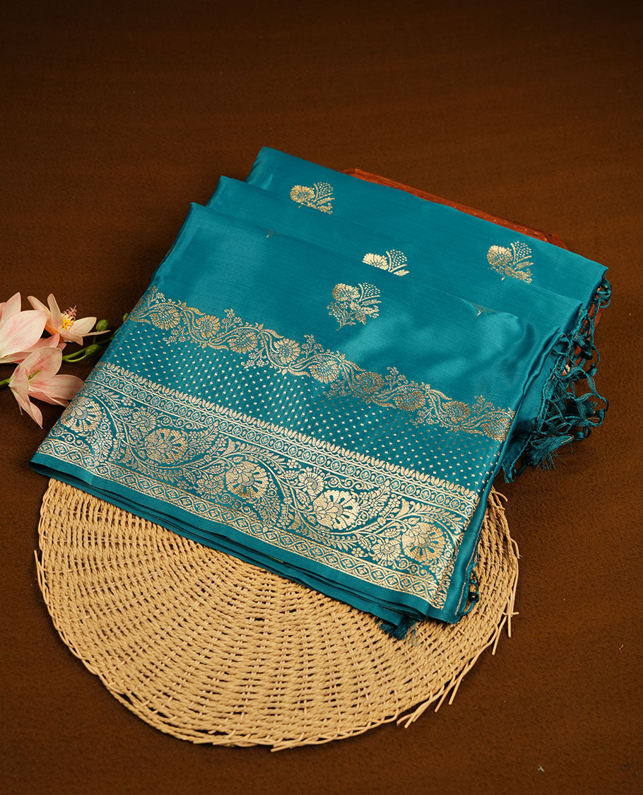 Teal blue colour Banaras Satin Crepe saree featuring gold zari floral motifs on the body, a richly woven traditional border with intricate gold zari detailing, and paired with a matching blouse.